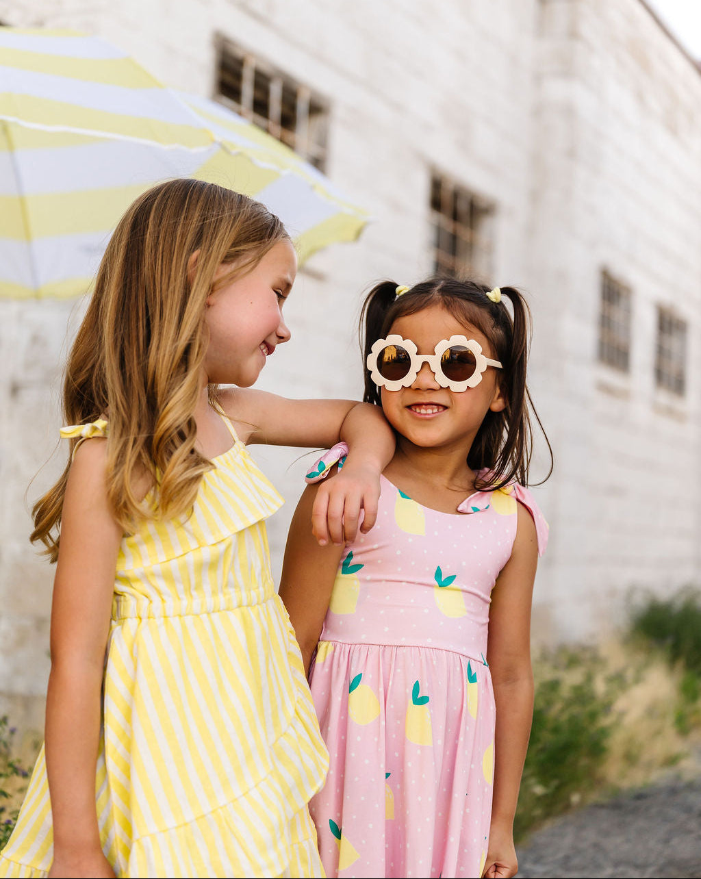 Two young girls in colorful dresses standing outdoors with a white building in the background.