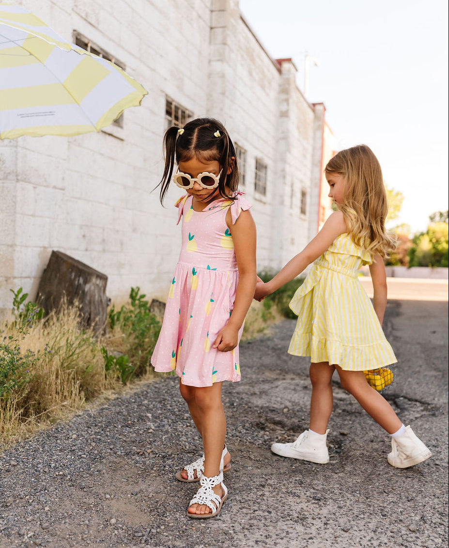 Two young girls in colorful dresses walking on a street with a white building in the background.
