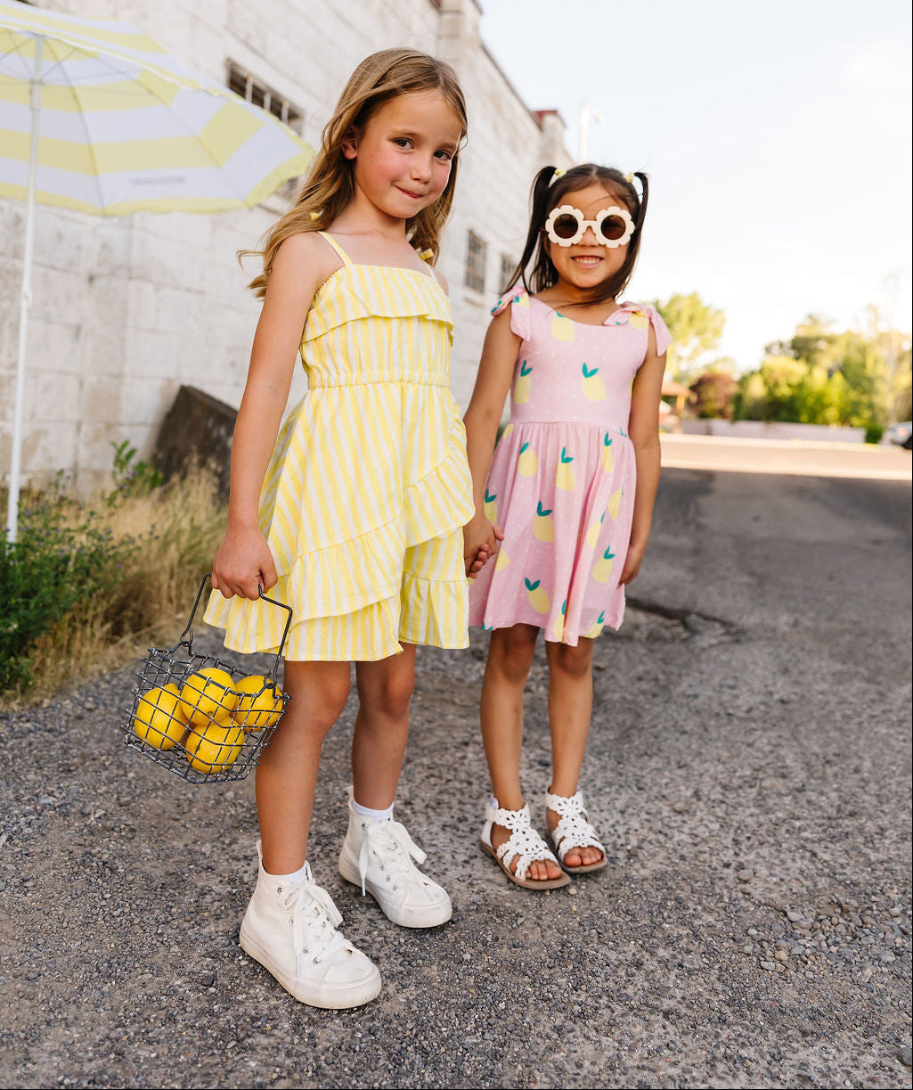 Two young girls in colorful dresses standing on a street with a building in the background.