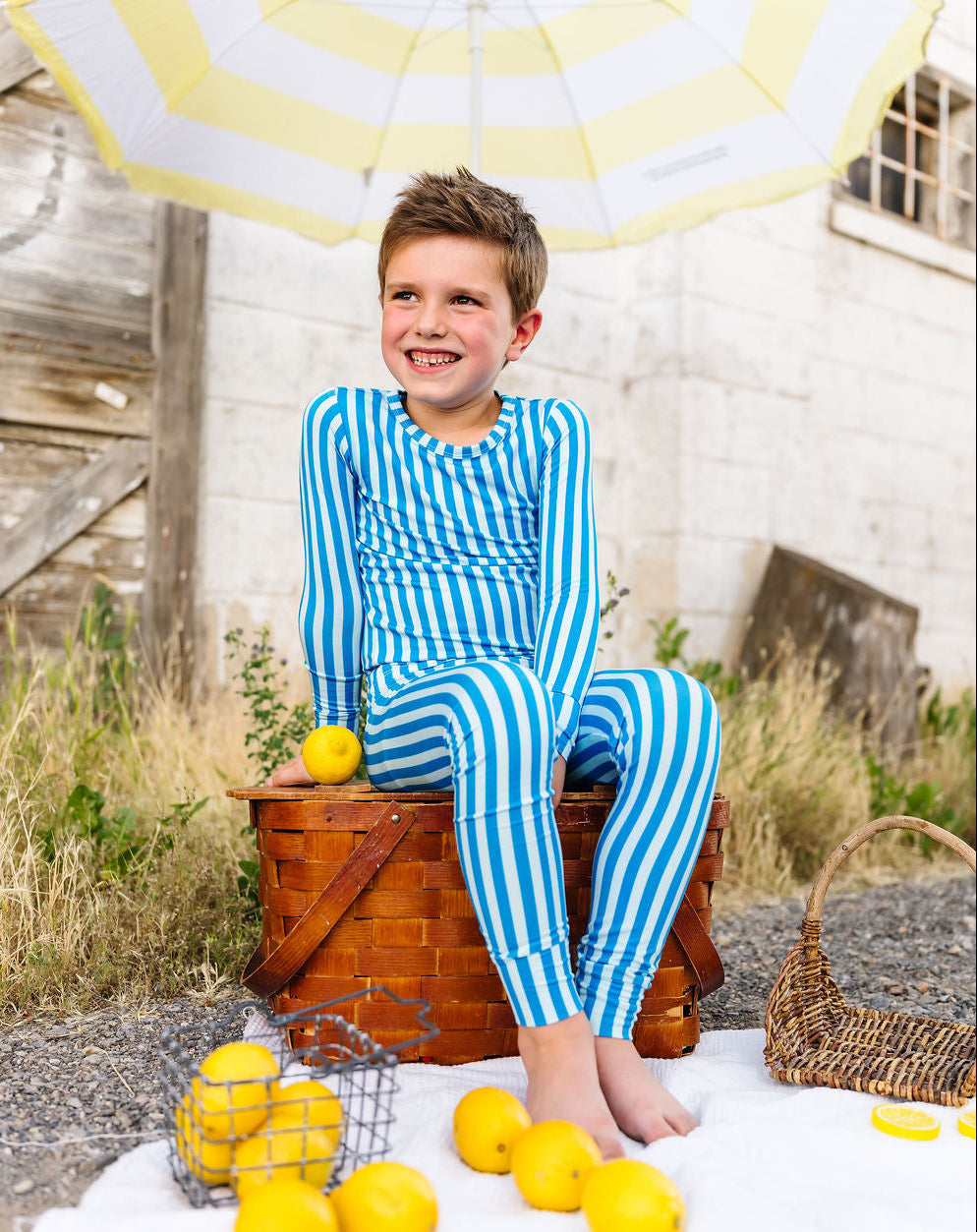 Child in blue striped pajamas sitting on a wooden barrel with lemons and an umbrella