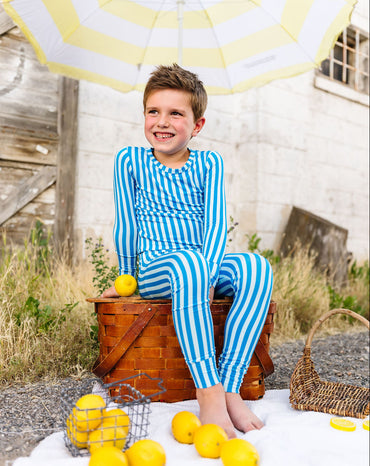 Child in blue striped pajamas sitting on a wooden barrel with lemons and an umbrella
