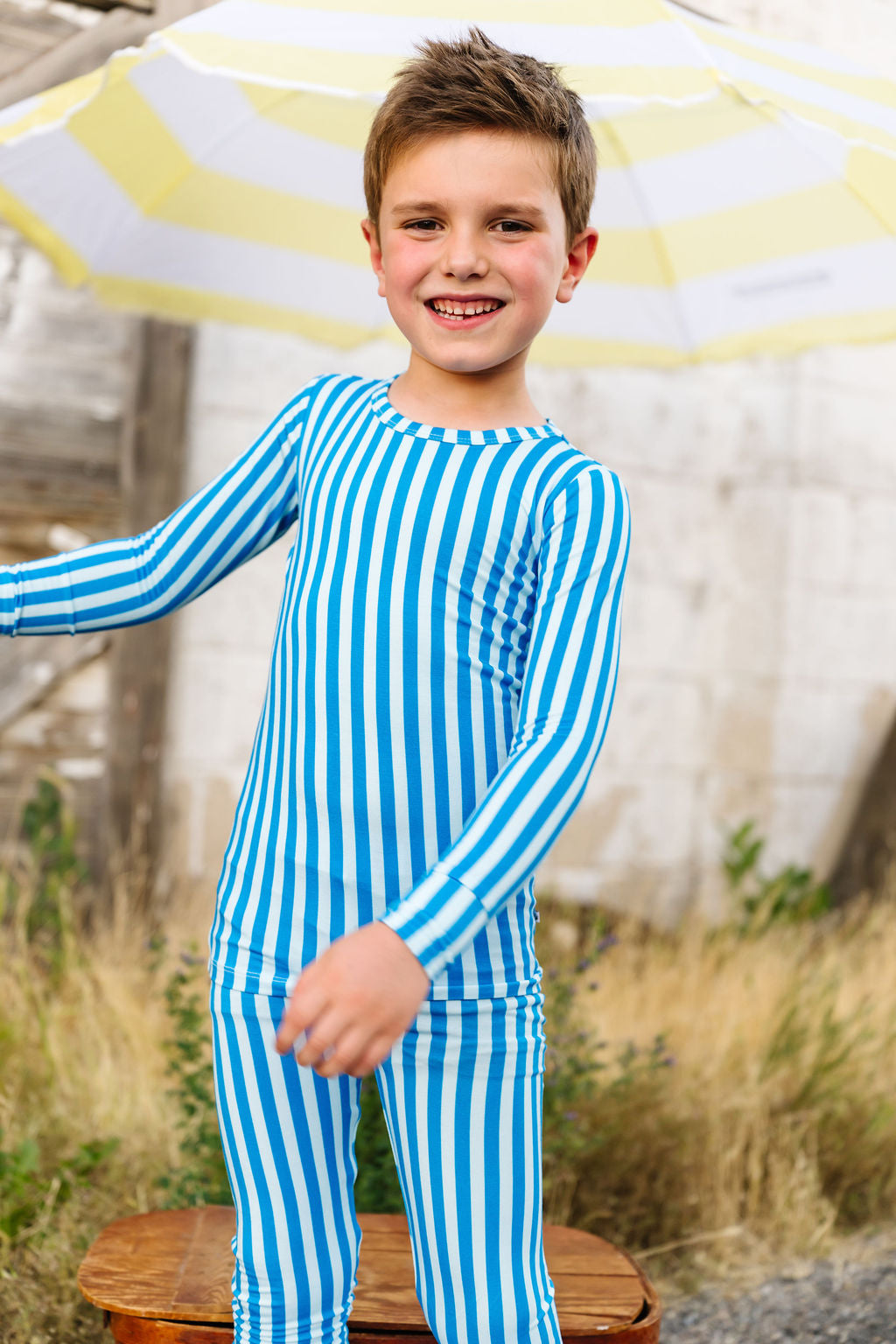 Child wearing a blue and white striped pajama set standing outdoors with a yellow and white umbrella.