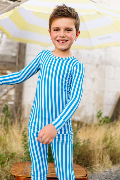 Child wearing a blue and white striped pajama set standing outdoors with a yellow and white umbrella.