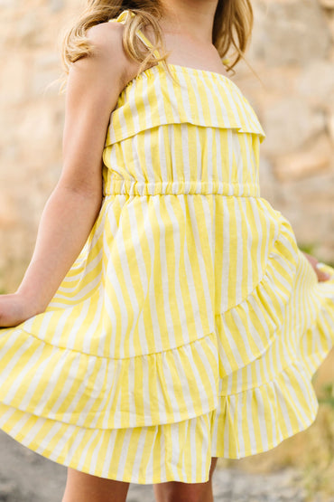Child wearing a yellow and white striped dress with a blurred natural background