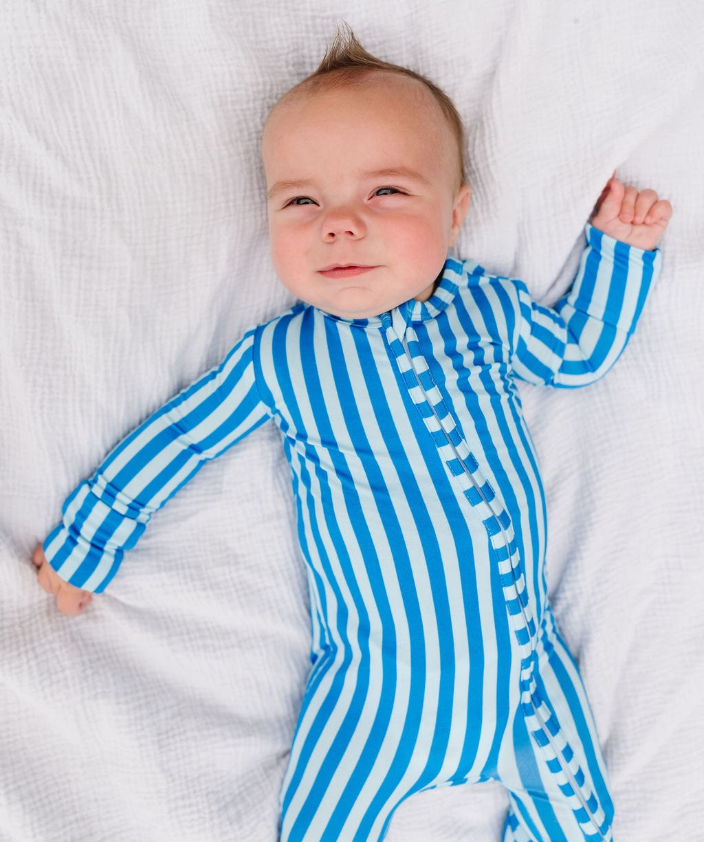 A baby lying on a white textured blanket, wearing a blue and white vertically striped long-sleeve footless onesie.