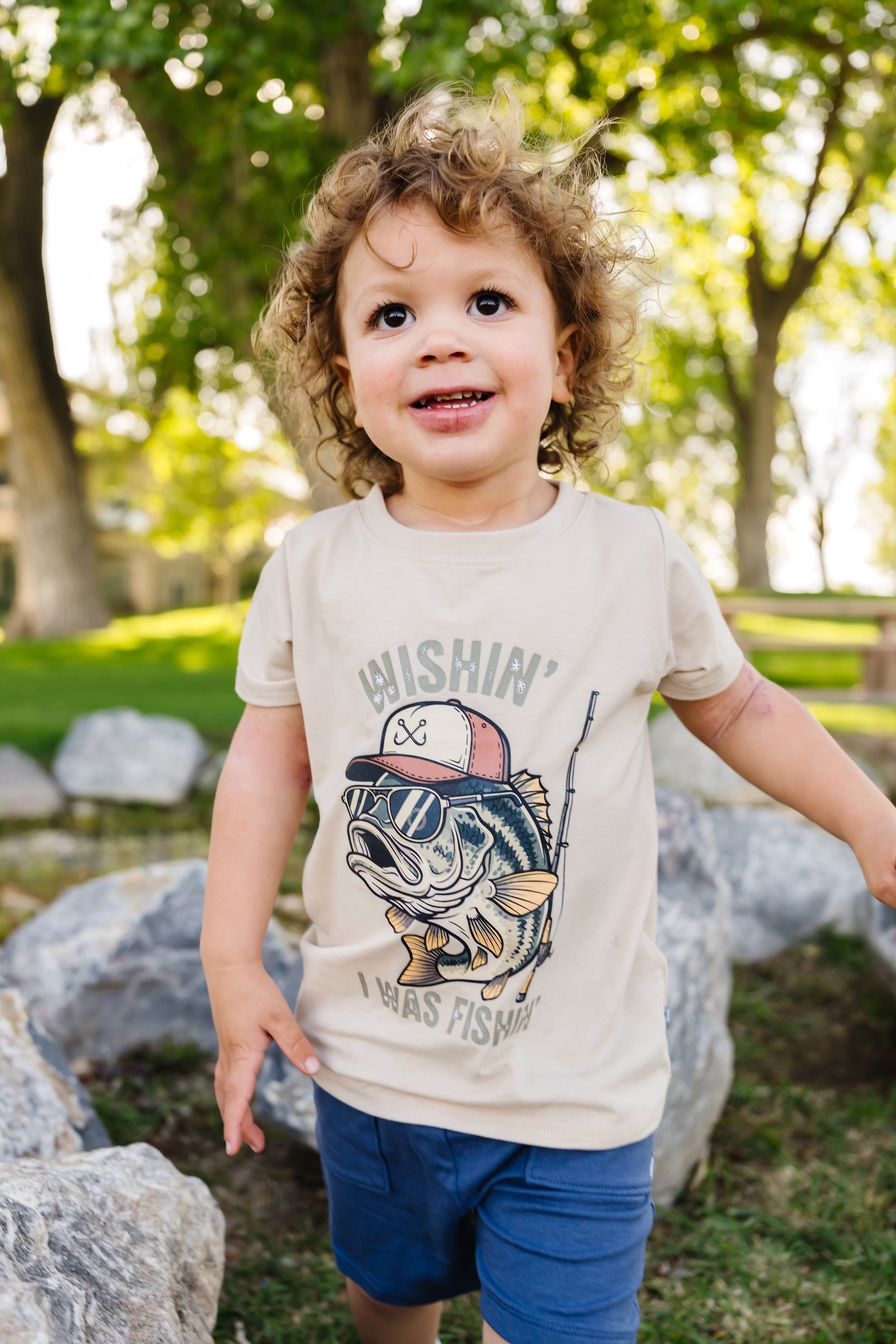 Child wearing a t-shirt with a fish graphic and text in a park setting