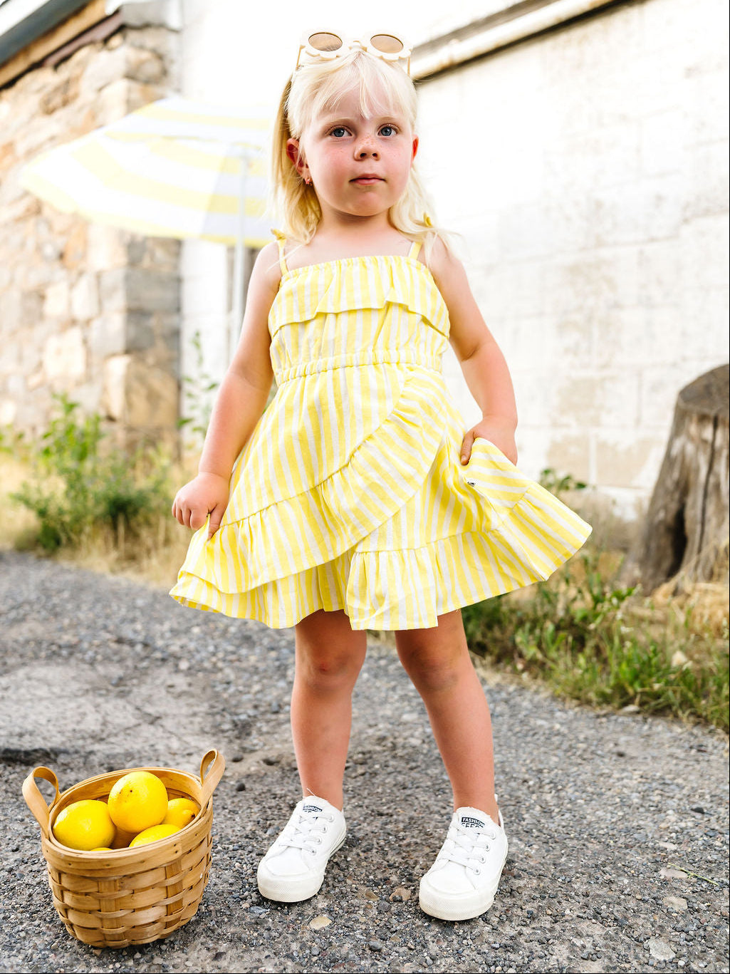 Young girl in a yellow dress standing outdoors with a basket of lemons.