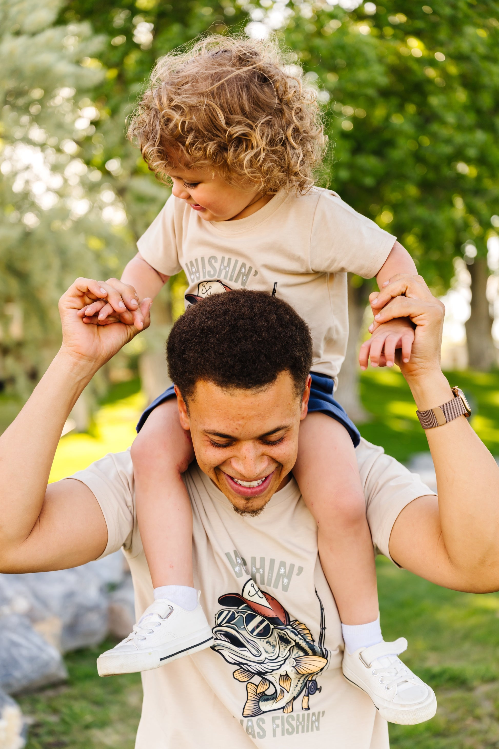Man carrying a child on his shoulders in an outdoor setting with greenery.