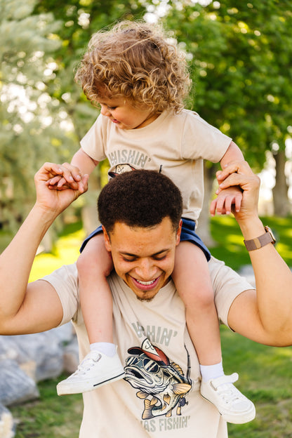 Man carrying a child on his shoulders in an outdoor setting with greenery.
