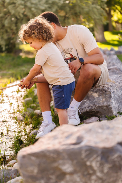 Man and child sitting on rocks by a stream, engaged in an activity.