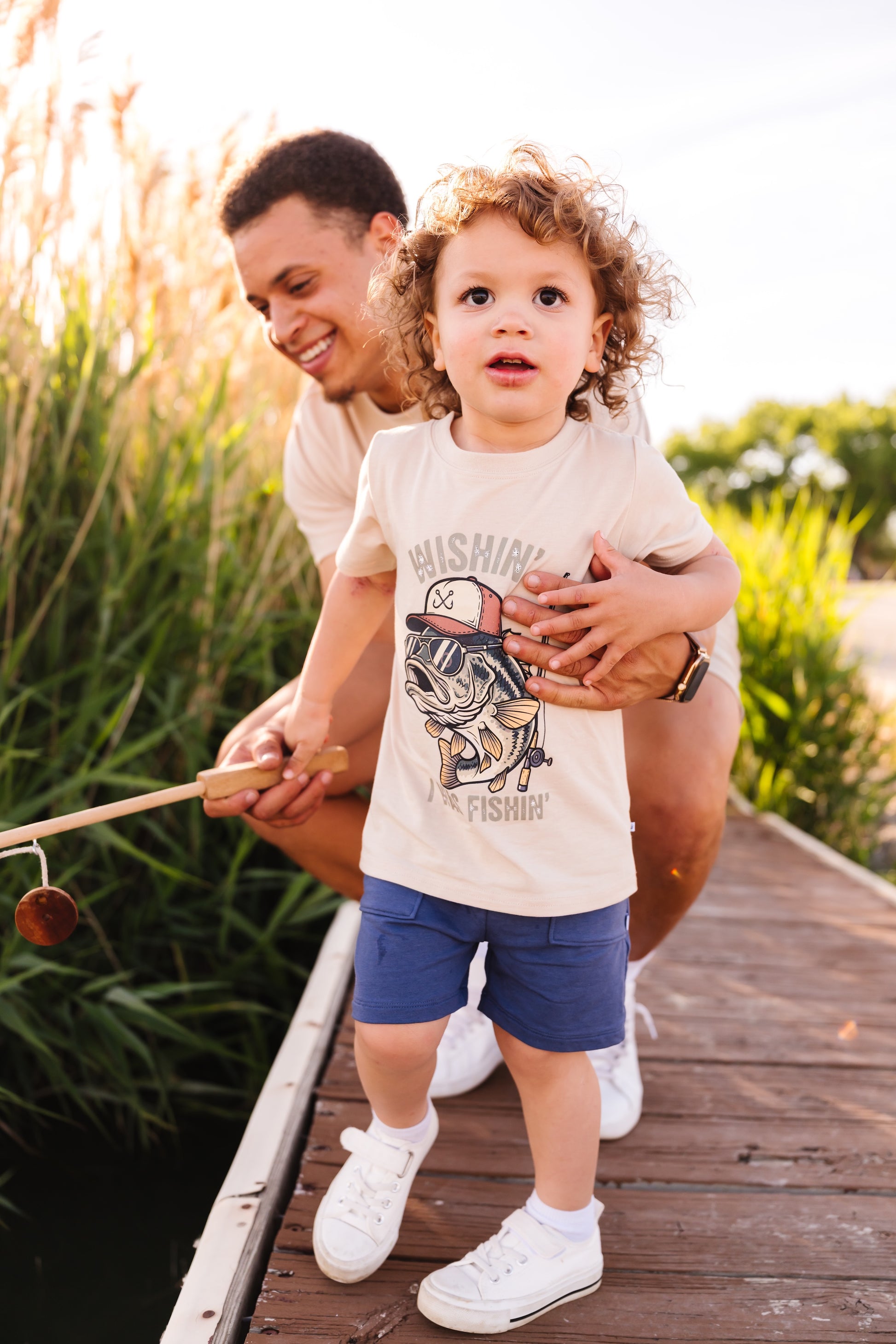 Man holding a child on a wooden dock with nature in the background