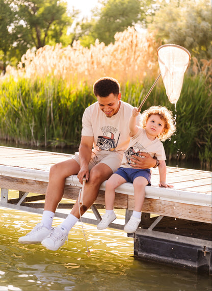 Man and child sitting on a dock by a body of water, holding a fishing net.