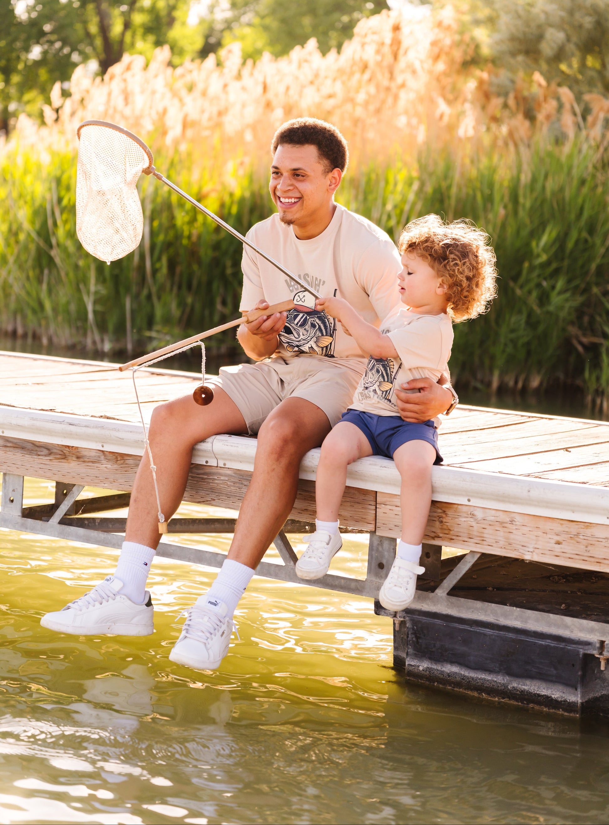 Man and child sitting on a dock by a body of water, with the man holding a fishing net.