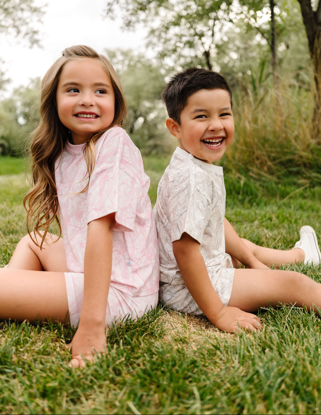 Two children sitting on grass with trees in the background