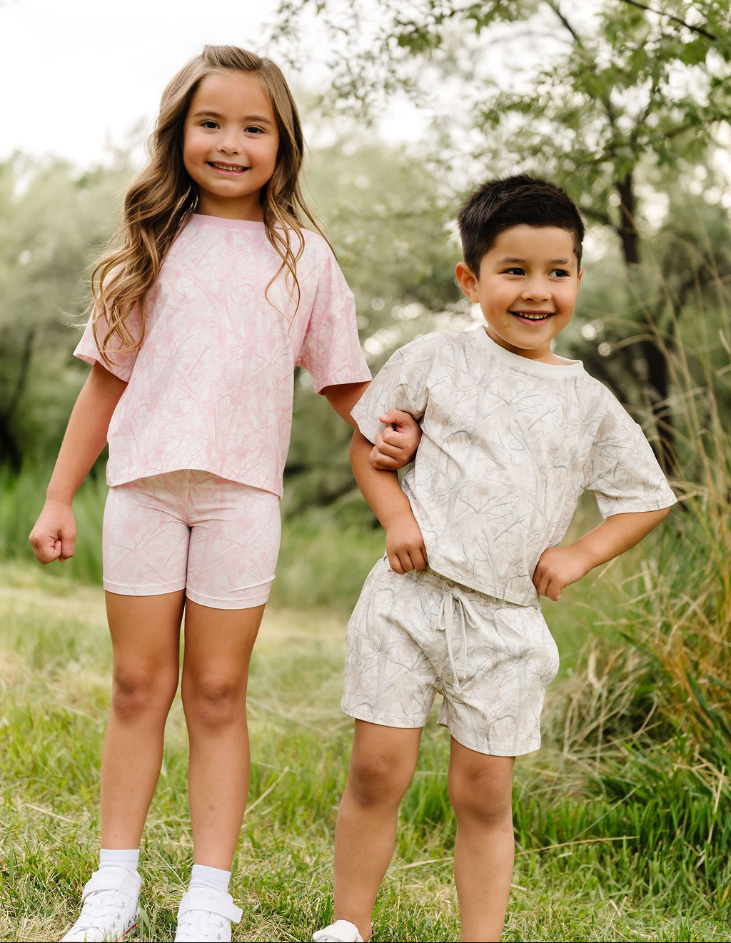 Two children standing in a grassy field with trees in the background