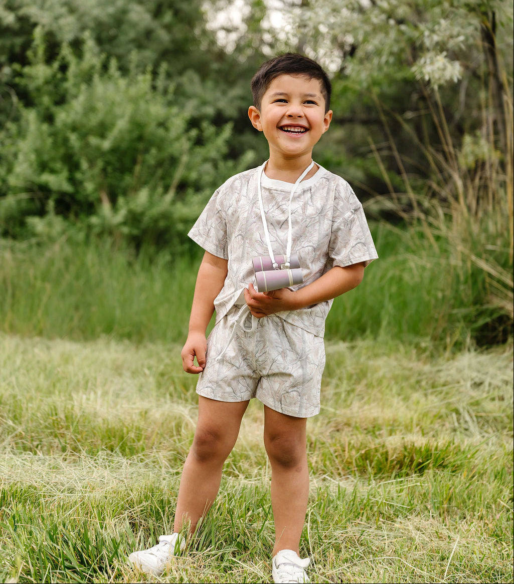 Child standing in a grassy field with trees in the background