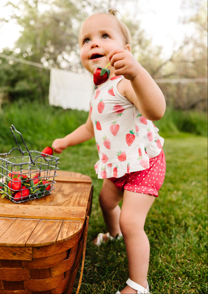 Child holding a strawberry outdoors near a wooden table with a basket of strawberries.