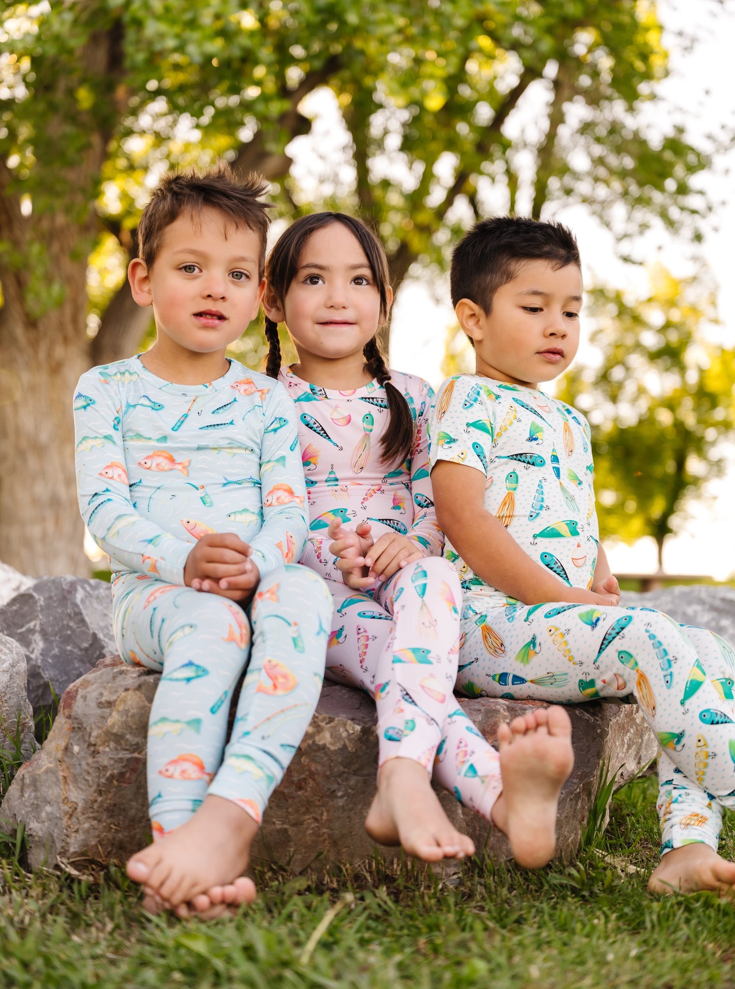 Three children wearing colorful pajamas sitting on a rock outdoors.