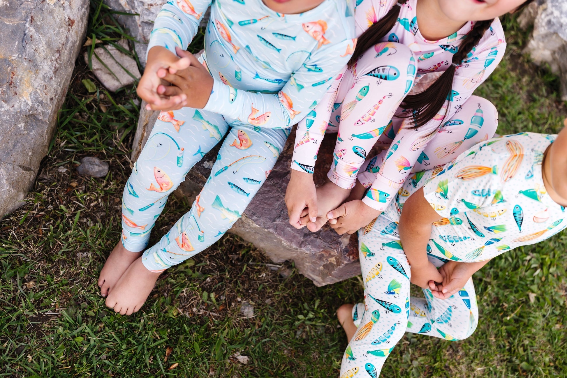 Three children wearing colorful pajamas sitting on a stone step outdoors.