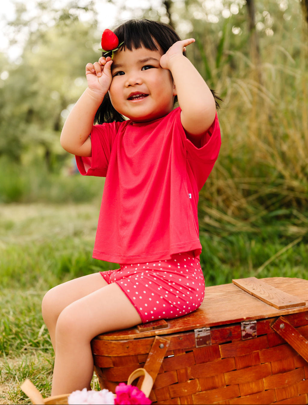 Child in a red outfit sitting on a wooden basket outdoors with a blurred natural background