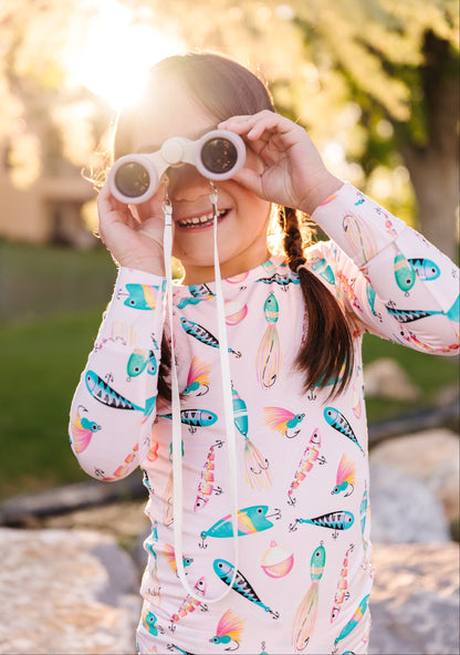 Child wearing  colorful long-sleeve pajamas with a fishing-themed design, holding binoculars outdoors.