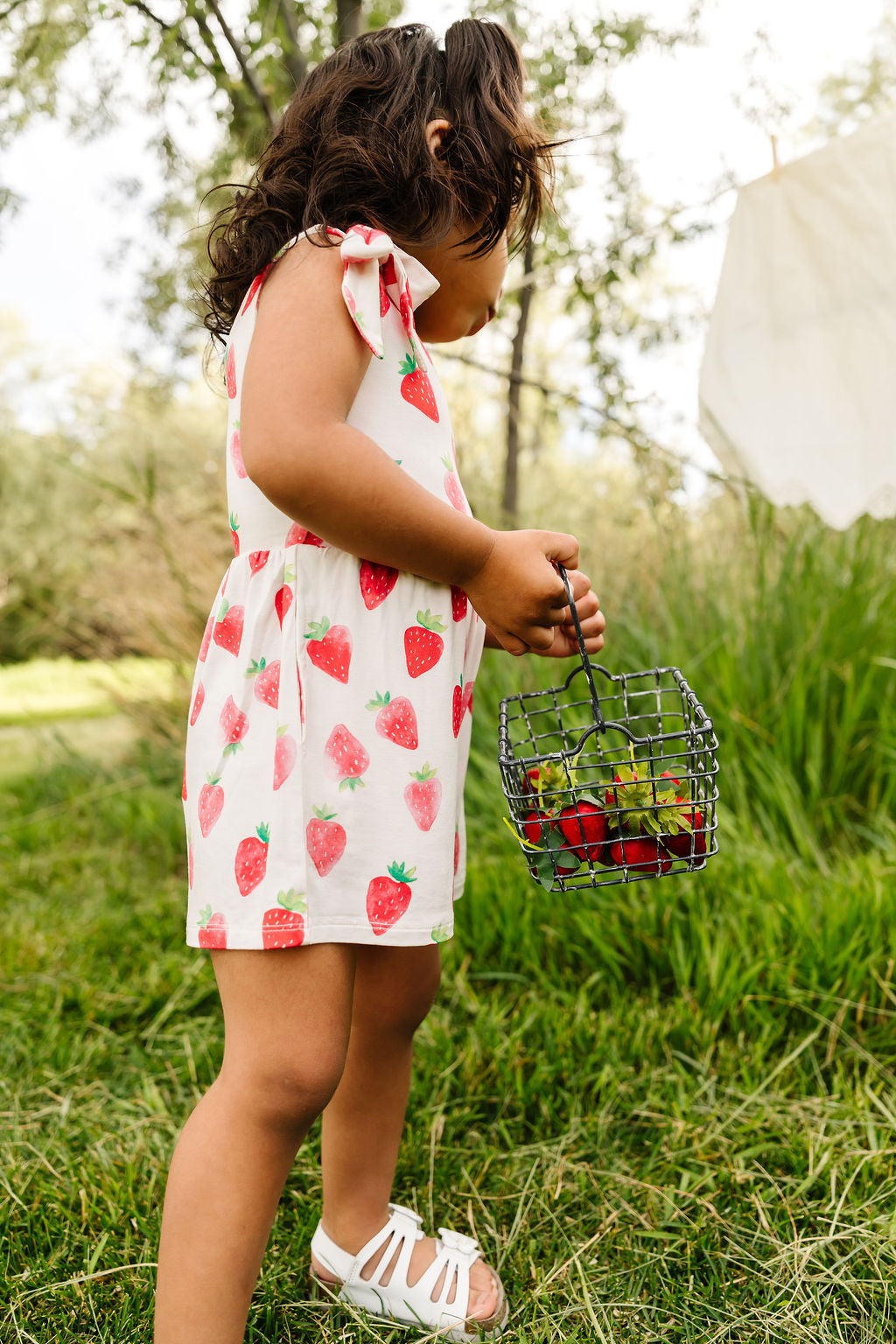 Child in a strawberry outfit holding a basket of berries in a natural setting