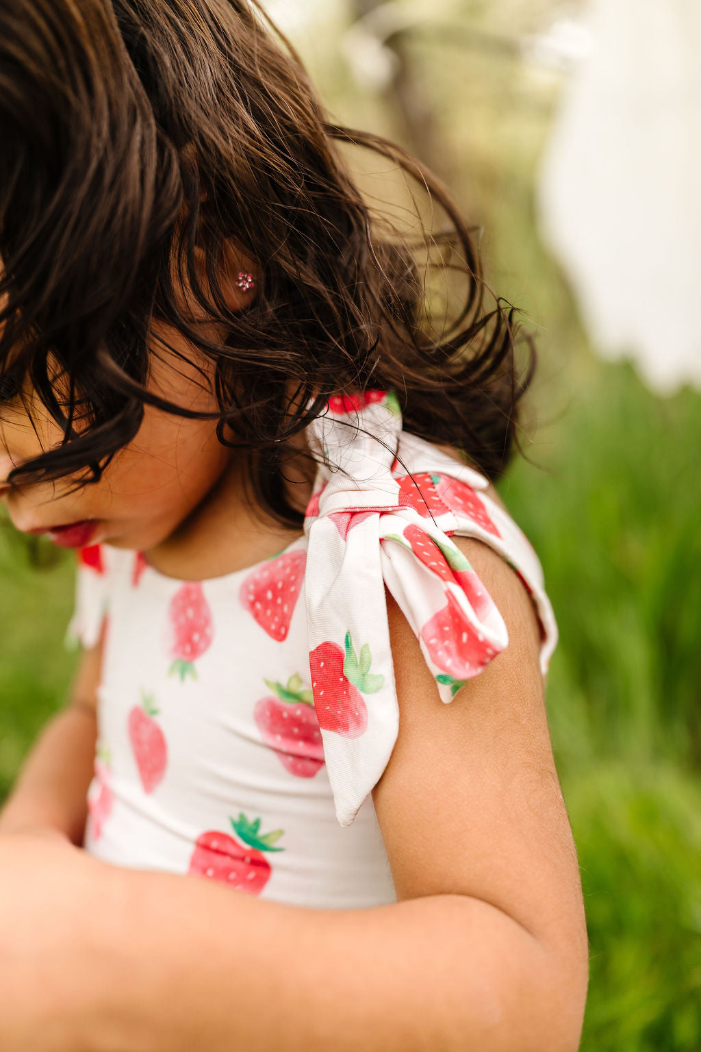 Child wearing a strawberry-patterned outfit with a bow in a natural setting