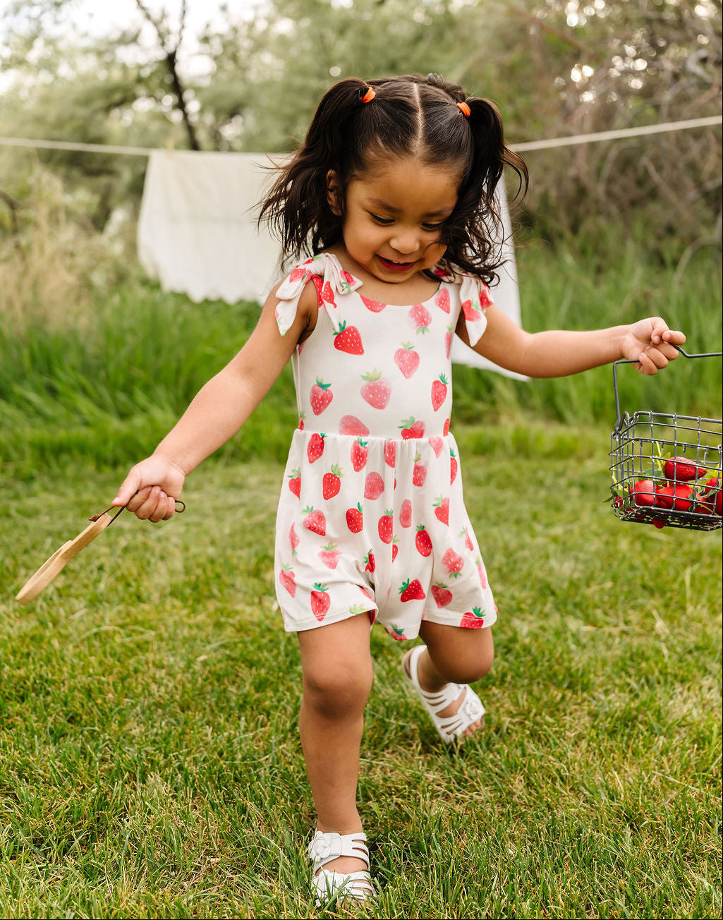 Child in a strawberry-patterned outfit running outdoors with a basket of strawberries.