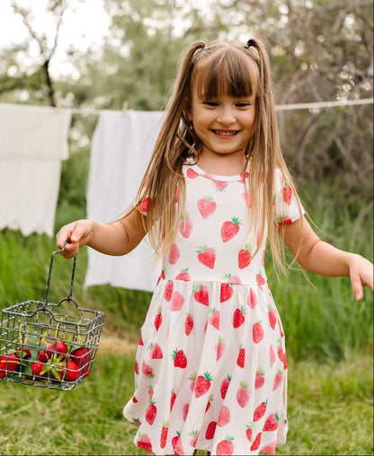 Young girl in a strawberry dress holding a basket of strawberries outdoors.
