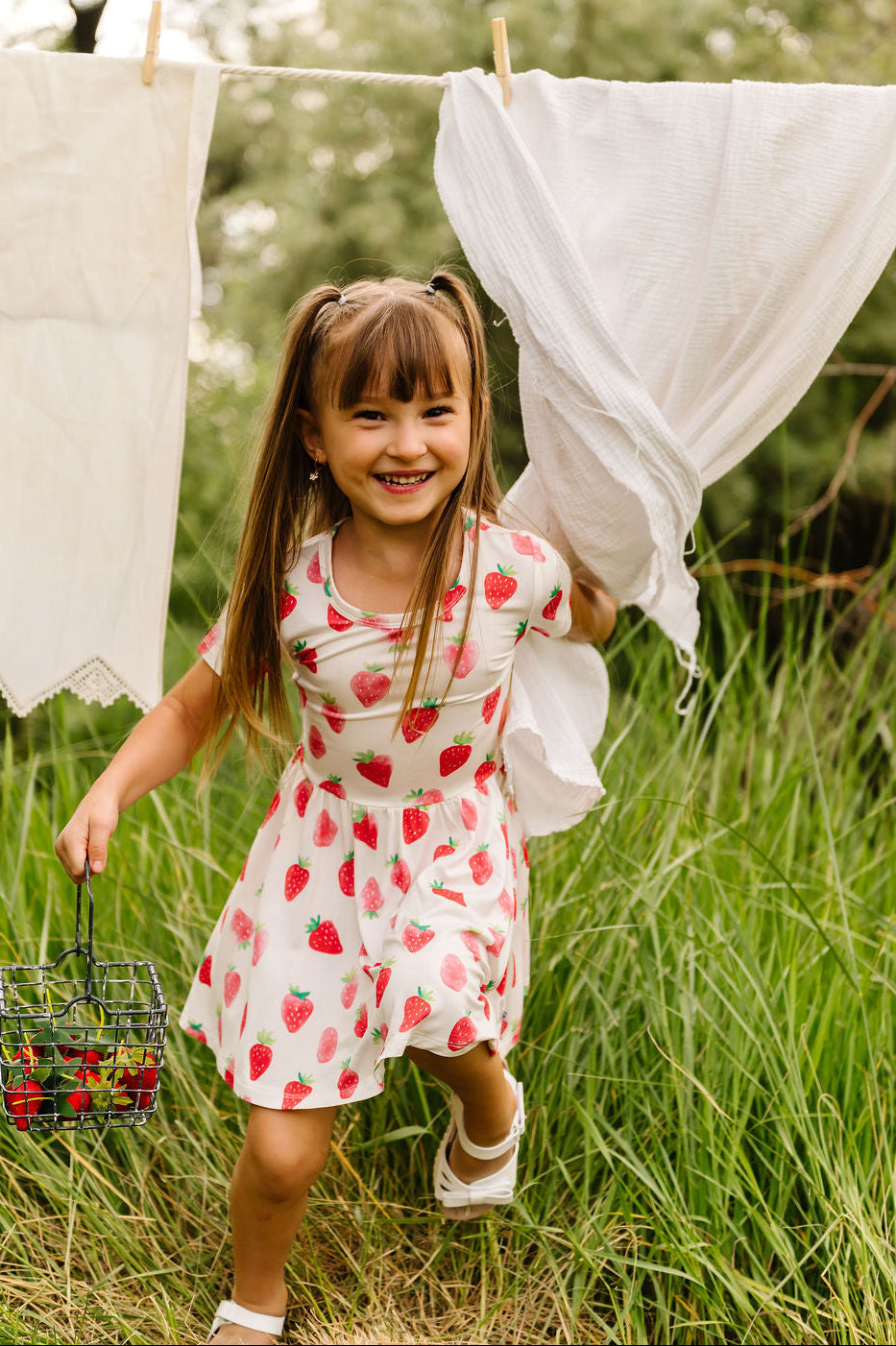 Young girl in a strawberry dress standing in grass with clothesline in the background