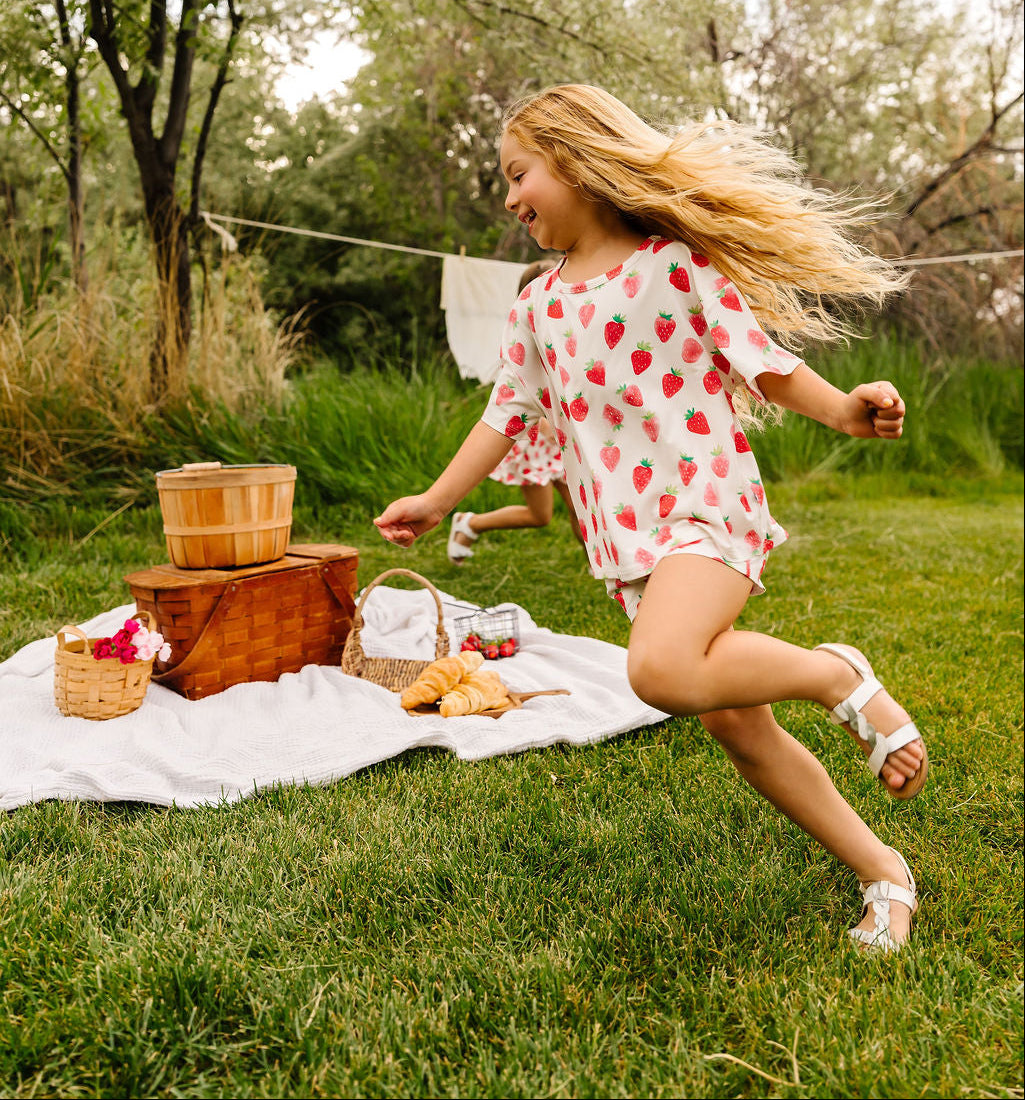 Young girl running on a grassy area with picnic items and trees in the background