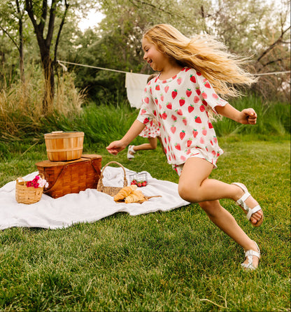 Young girl running on a grassy area with picnic items and trees in the background