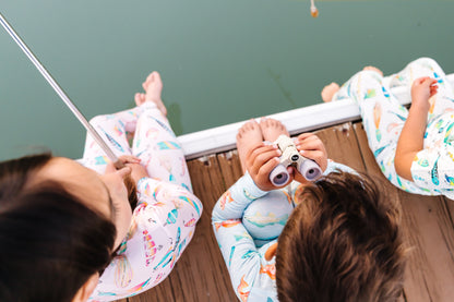 Children in pajamas looking through binoculars on a wooden dock.