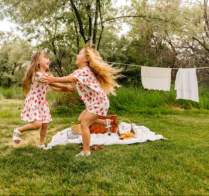 Two girls in strawberry outfits dancing outdoors with a picnic basket and blanket