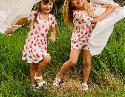 Two young girls in matching outfits running through a grassy field.