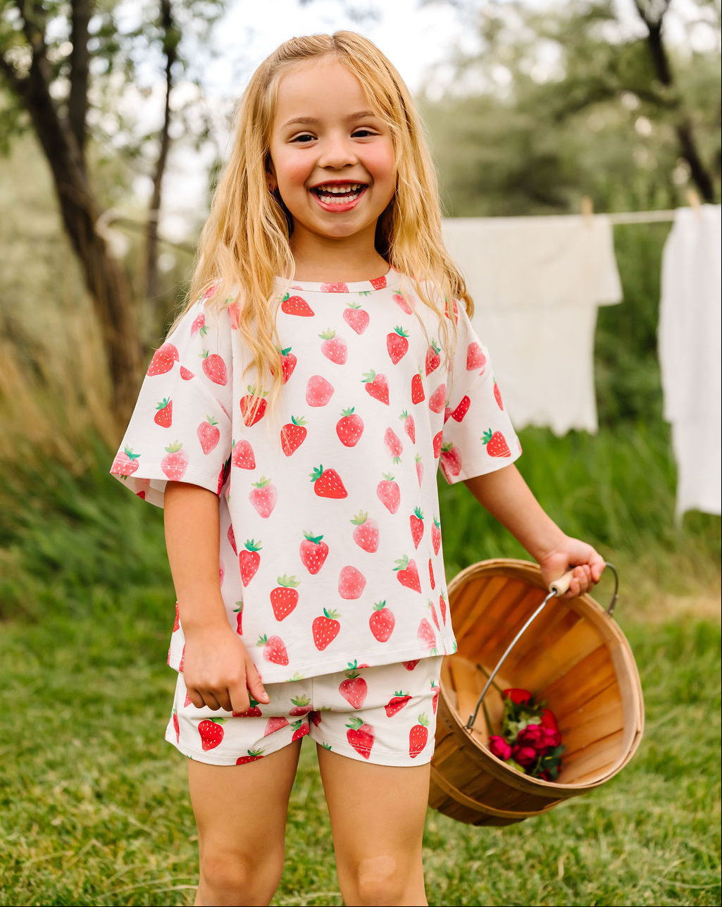 Young girl in strawberry-patterned outfit holding a basket outdoors