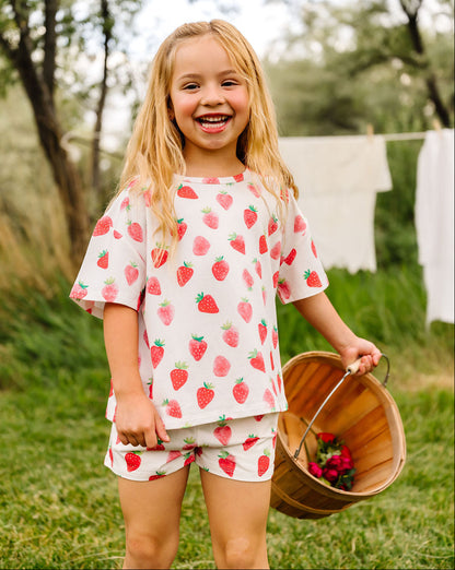 Young girl in strawberry-patterned outfit holding a basket outdoors