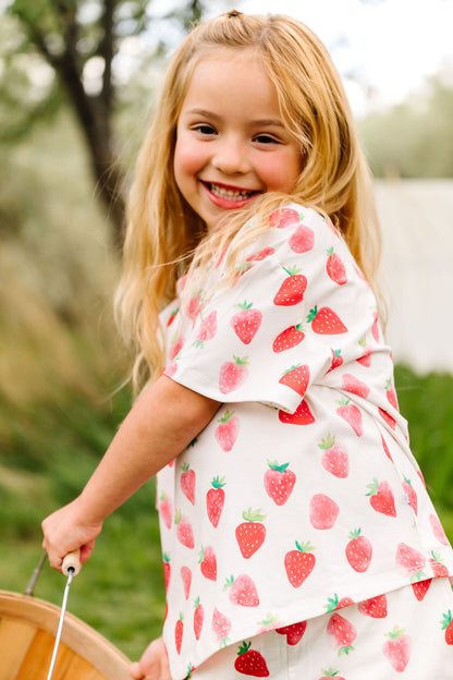Young girl wearing a strawberry-patterned outfit outdoors
