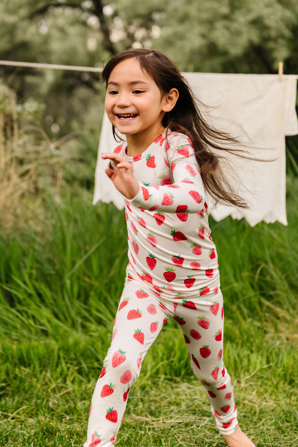 Child wearing strawberry-patterned pajamas standing in a grassy outdoor area.