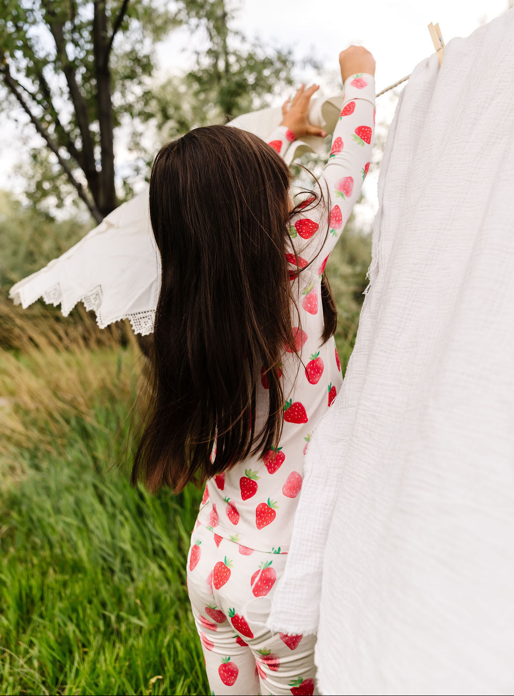 Girl wearing a strawberry-patterned pajama set standing outdoors with trees and grass in the background