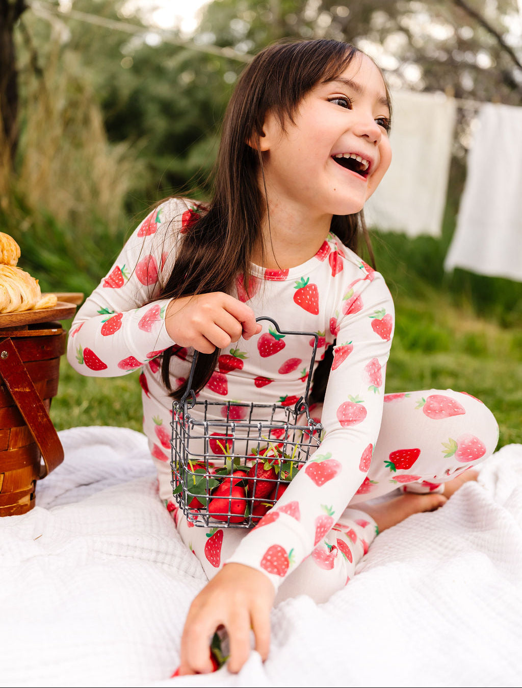 Child wearing a strawberry print pajama set sitting outdoors on a blanket.