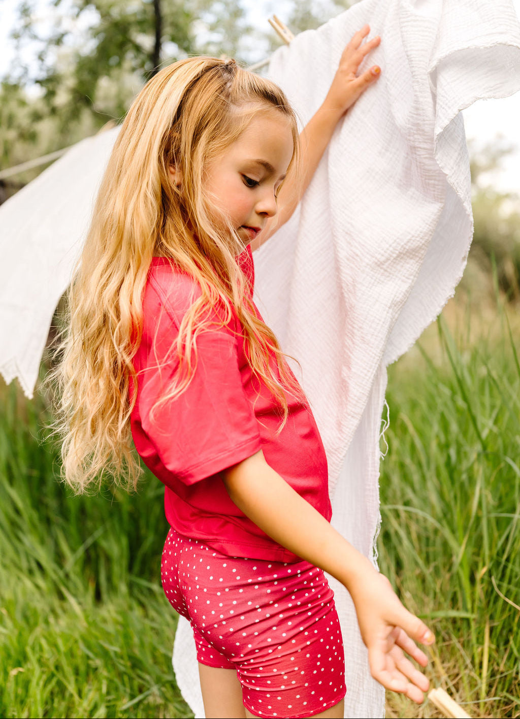 Young girl in a red outfit standing in a grassy field with a white sheet.