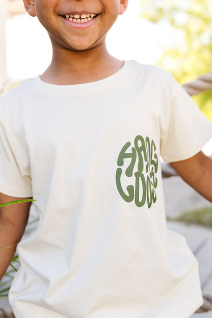 Child wearing a white t-shirt with green text outdoors