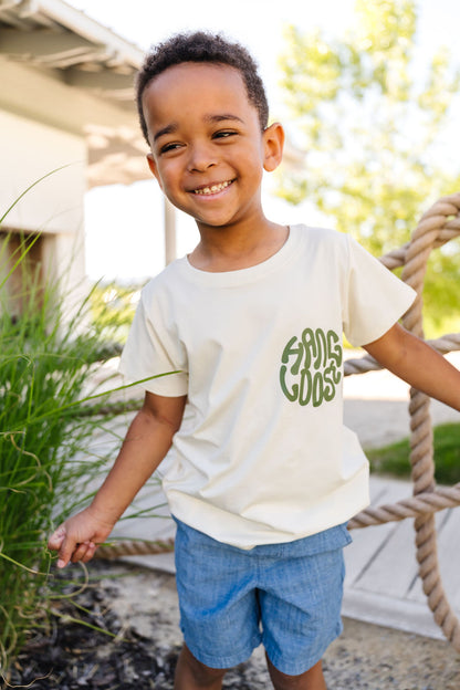 Child wearing a white t-shirt with green text, standing outdoors.