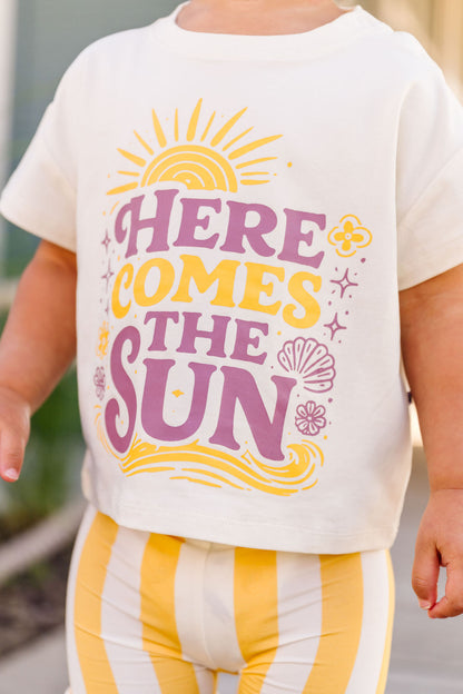 Child wearing a shirt with 'Here Comes the Sun' text and graphics.