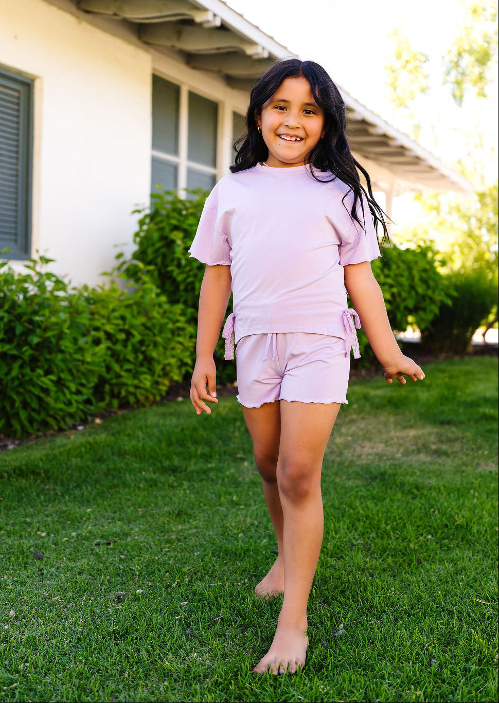 Young girl in a purple outfit standing on grass in front of a house