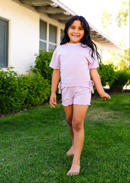 Young girl in a purple outfit standing on grass in front of a house