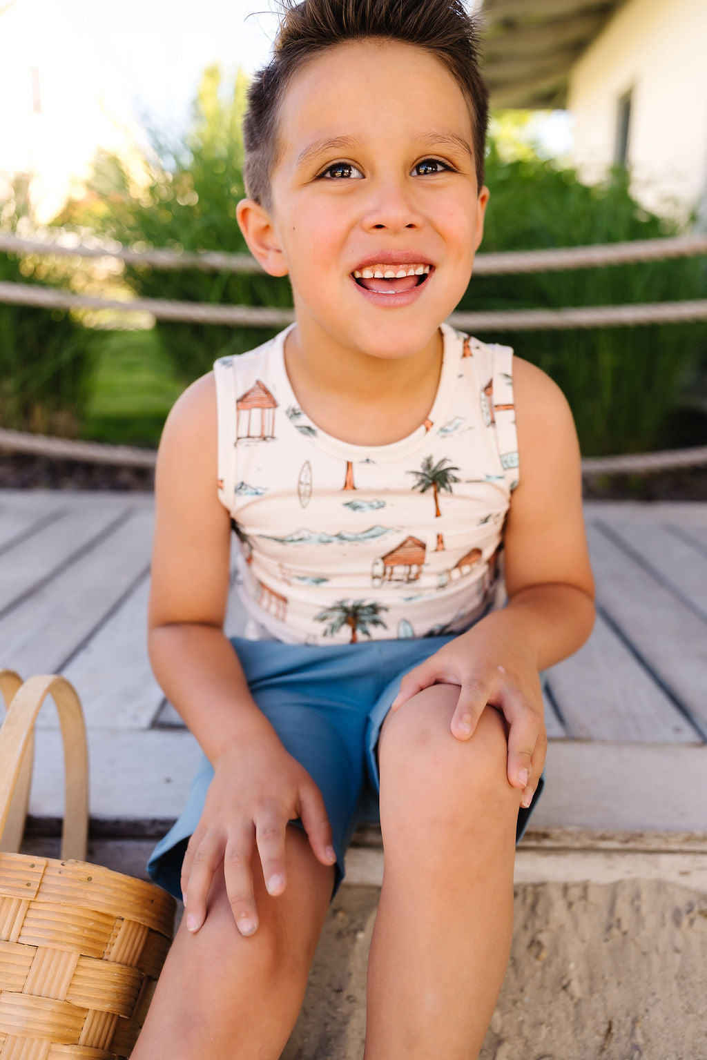 Child sitting outdoors wearing a sleeveless shirt with a palm tree design.