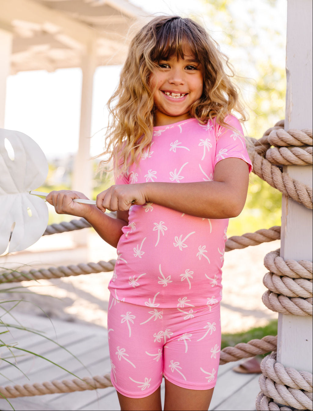 Young girl in a pink palm tree patterned outfit standing on a dock.