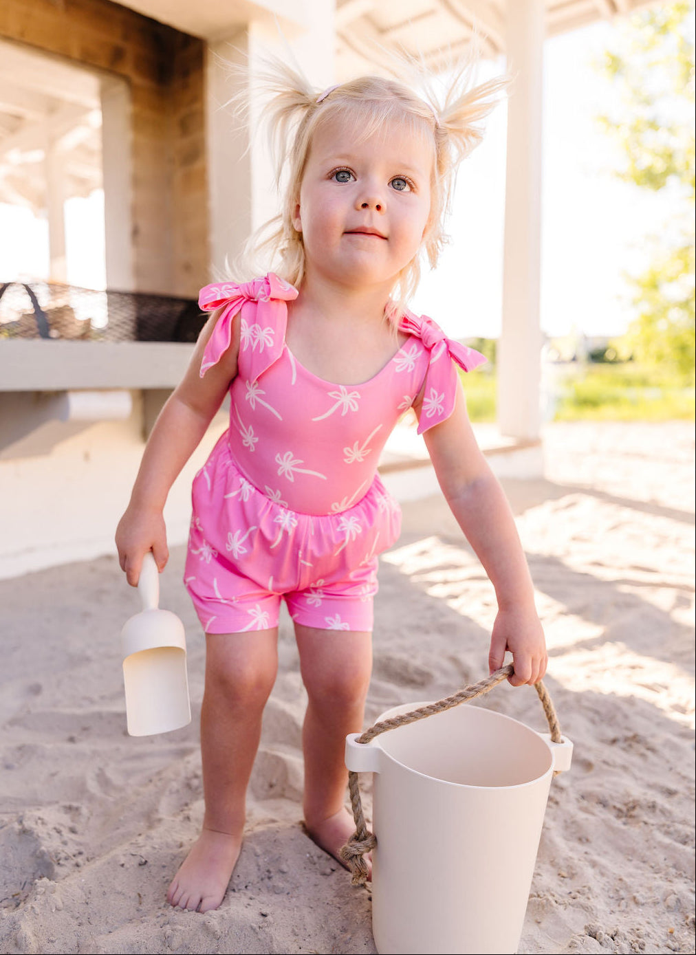 Young girl in a pink romper playing on a sandy beach.
